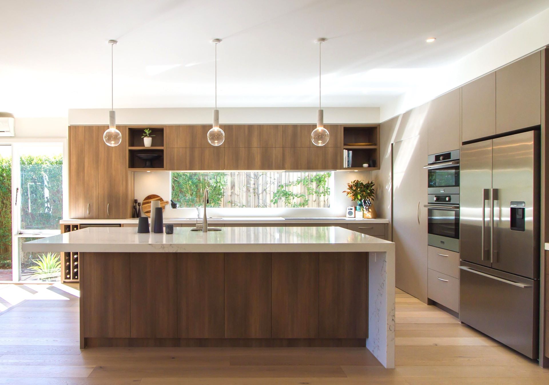 Mix of modern glass light, wooden flooring, wood cabinetry, and metallic kitchen appliances in Contemporary kitchen