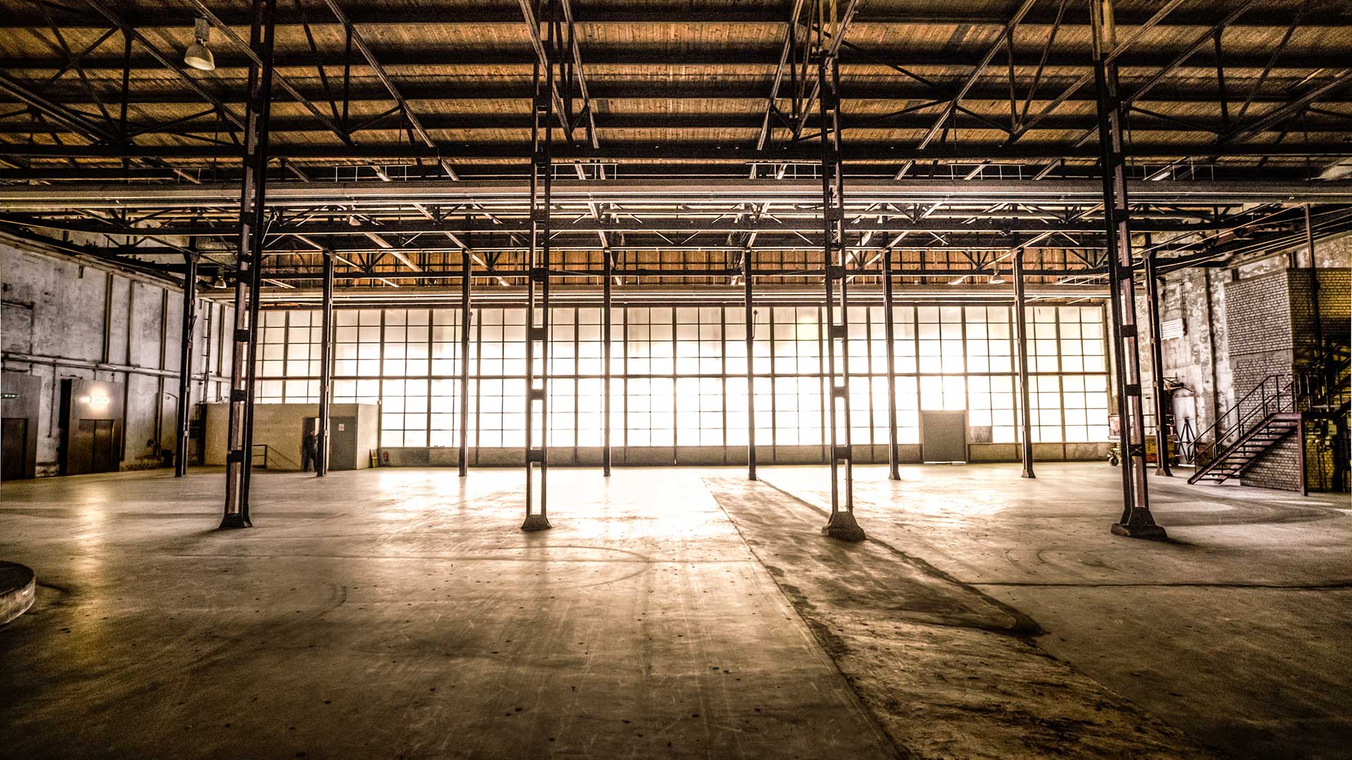 A deserted factory space with exposed pipes, brick walls, metallic pillars, and Industrial materials