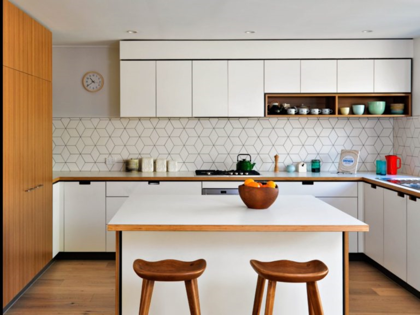 Plain white kitchen with island and wooden stools stocked with dinnerware in teal shades