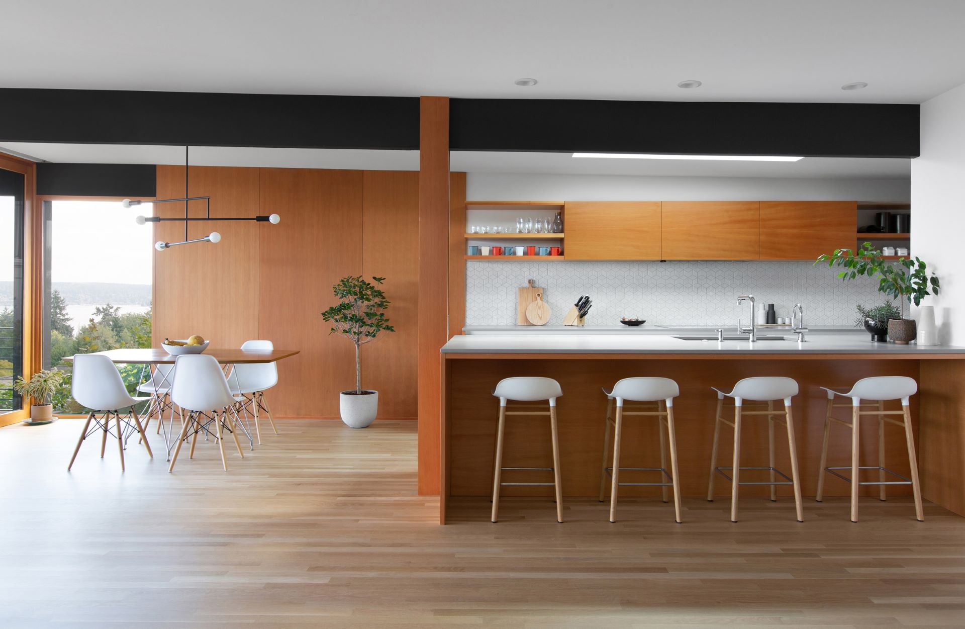  Open kitchen and dining area in darker shades of wood with white chairs and stools matched with metal lights