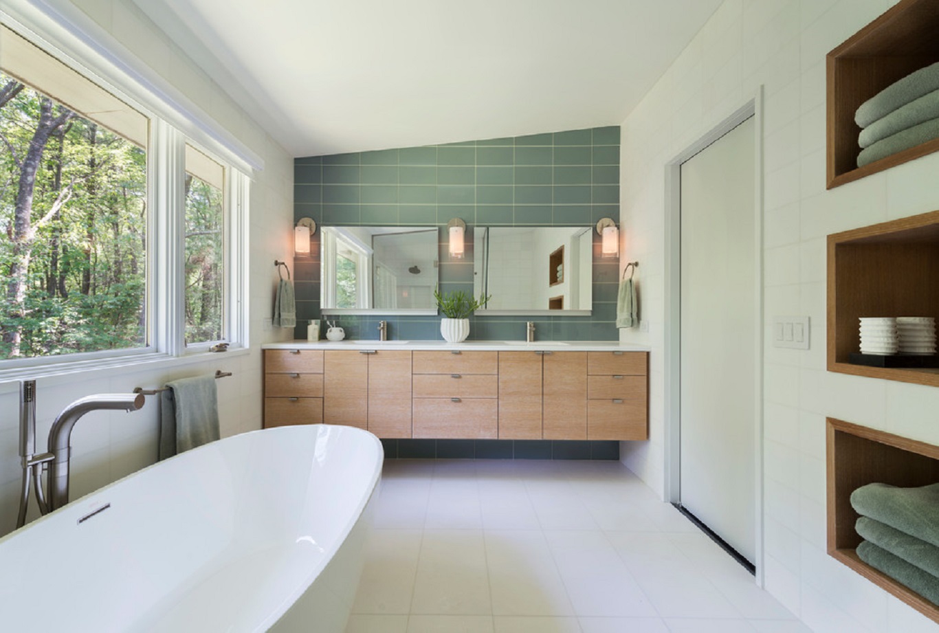 Standalone bathtub in whitewashed bathroom matched with wooden cabinets and various teal elements