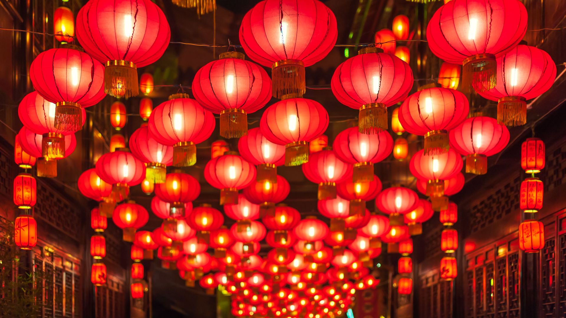 Many red traditional Chinese lanterns hanging above the middle of a small Chinese town walkway