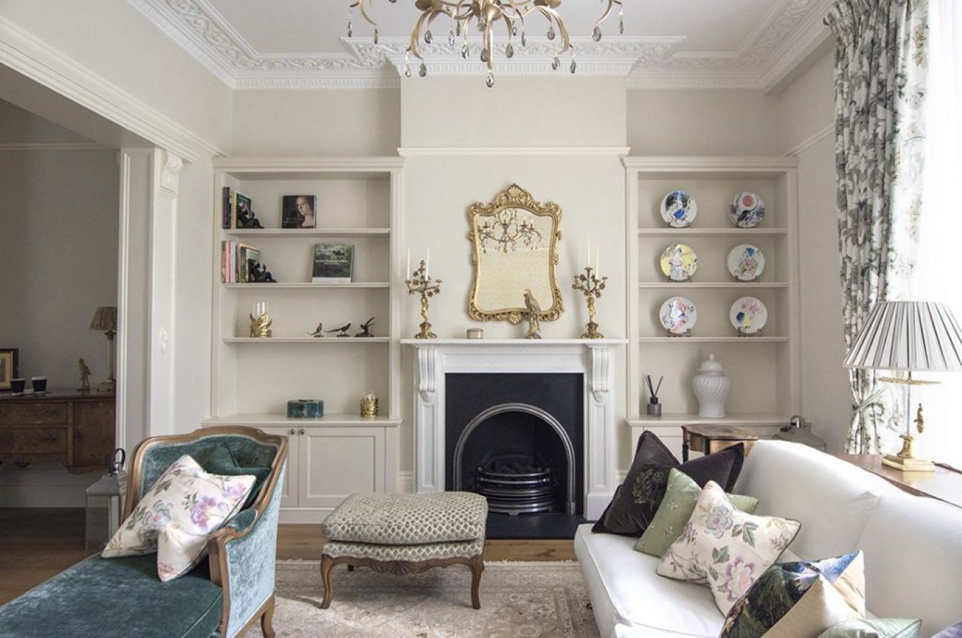 Victorian living room with chaise lounge, floral cushions  and ornately-carved mirror on wall.