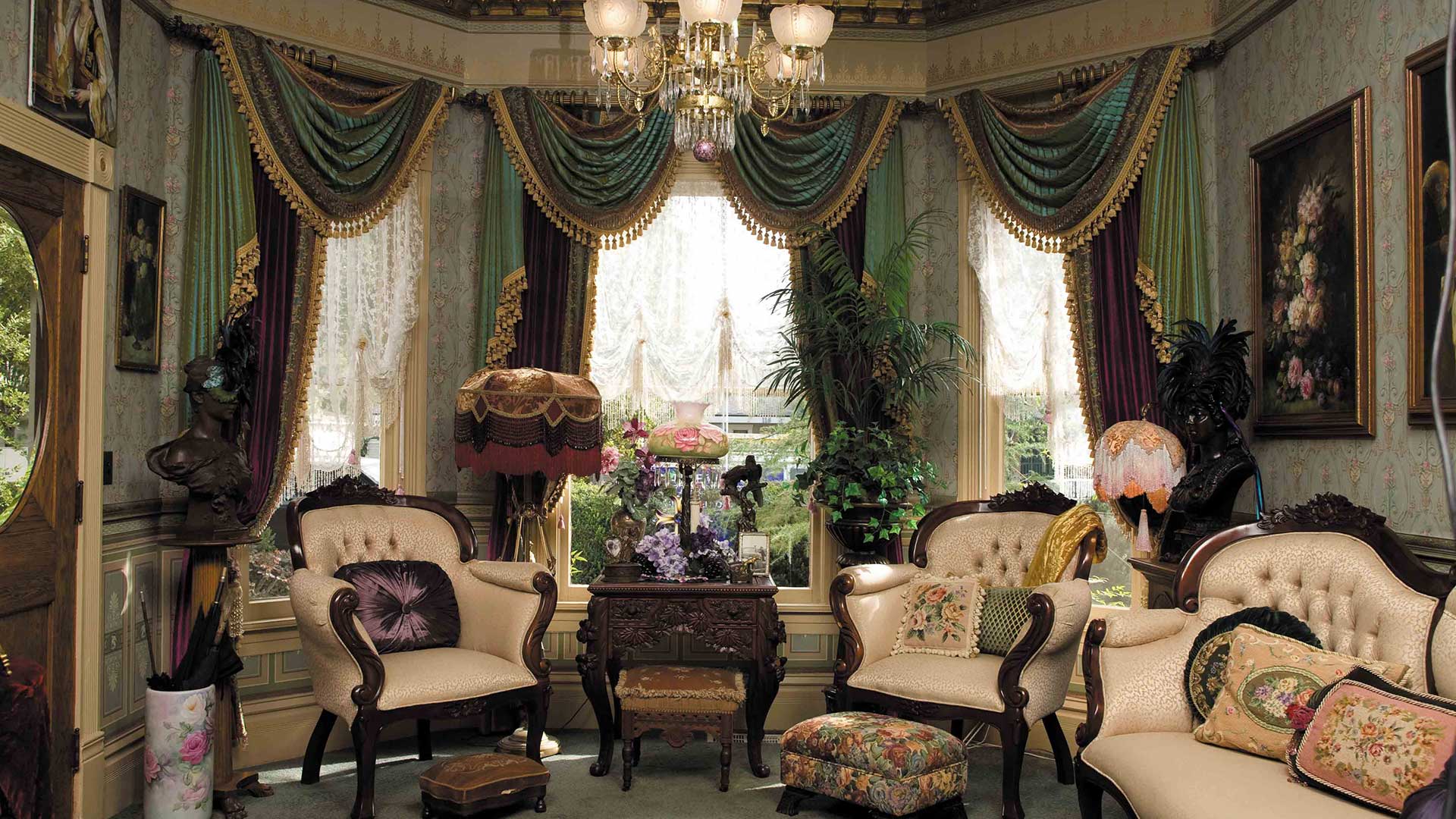 Aristocratic-style living room portraying Victorian decor, floral wallpaper, ornate furniture, and a chandelier.