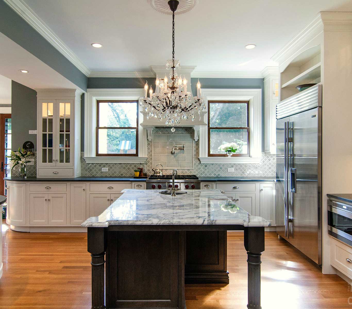 Kitchen with polished wooden flooring, center marble-top island with over-hanging crystal pendant light.