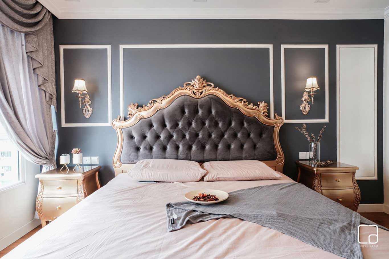 Large master bed with ornate quilted headboard against a backdrop of grey-toned walls. 