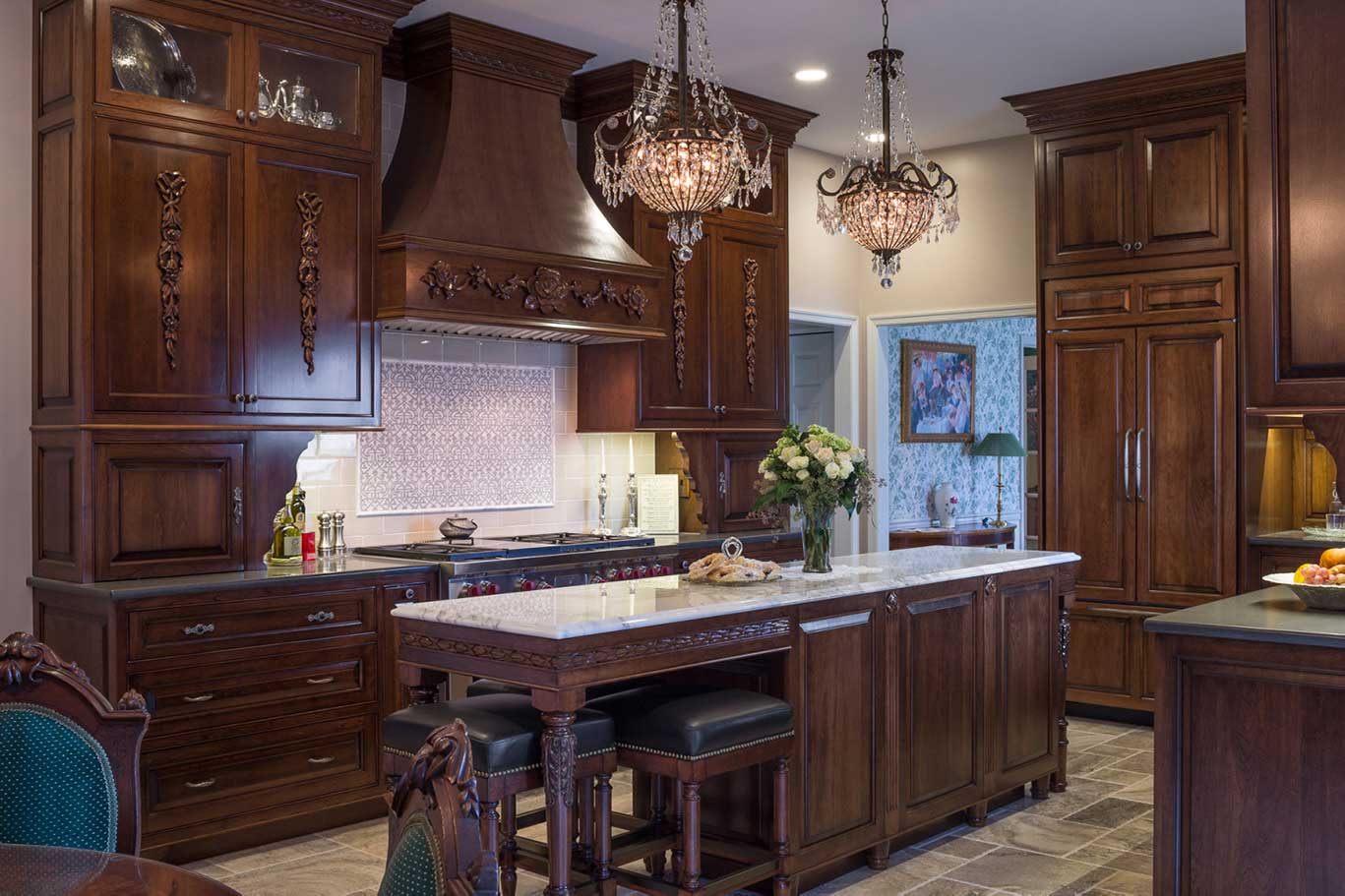 A glass vase with a bouquet of flowers, pendant chandeliers and hand-carved wood in a Victorian design kitchen.