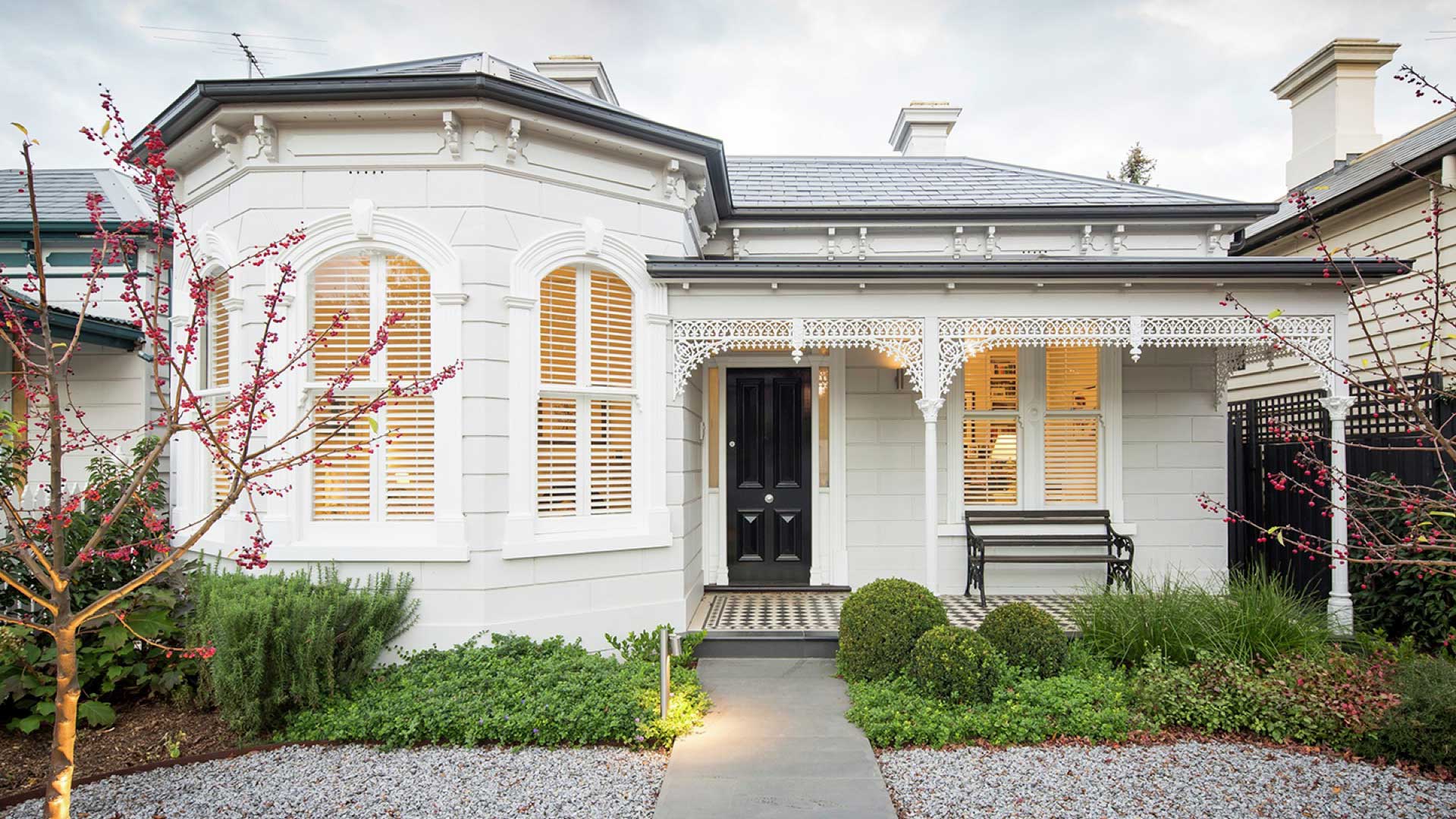 White colonial-style house exterior with bow windows overlooking garden patch.